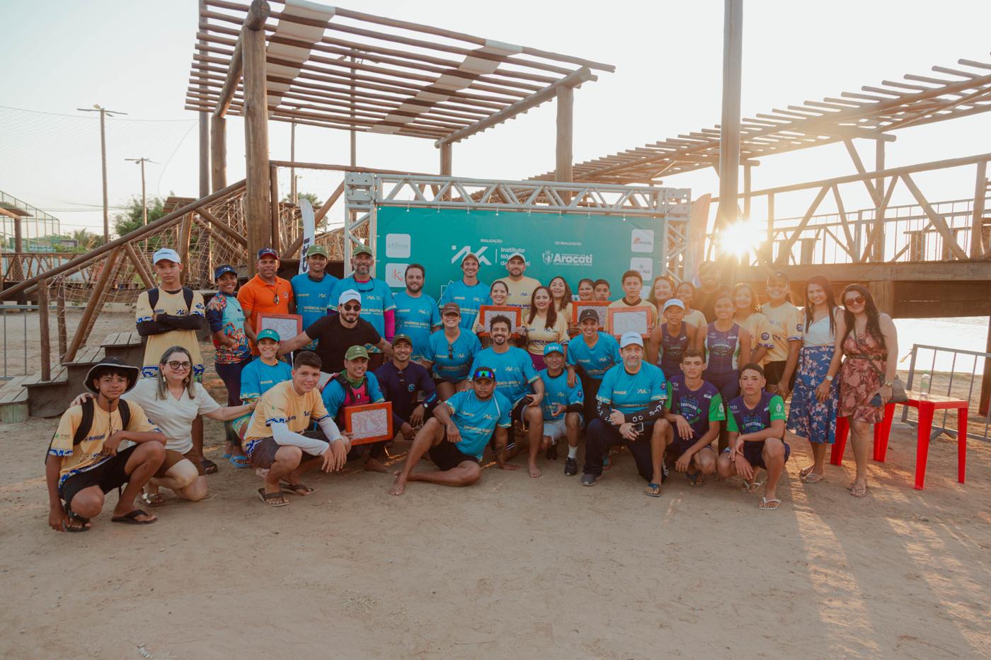 Equipe e participantes da 1ª Vivência Náutica reunidos em frente ao painel do evento