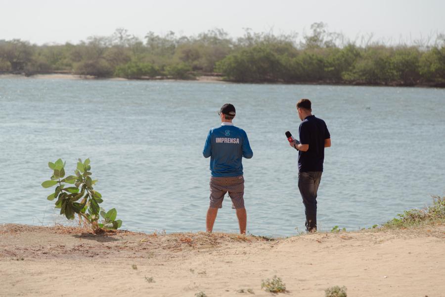 Duas pessoas na margem do rio ao lado de uma muda de mangue
