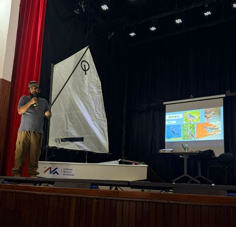 Palestrante fala sobre o estuário ao lado de um barco Optimist no palco