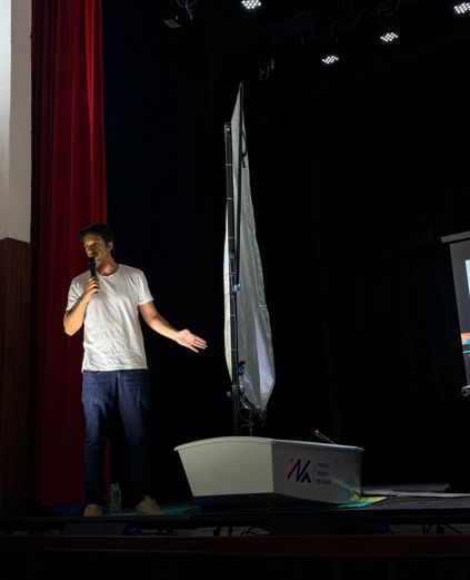 Palestrante apresenta ao lado de um Optimist com o logo do INA